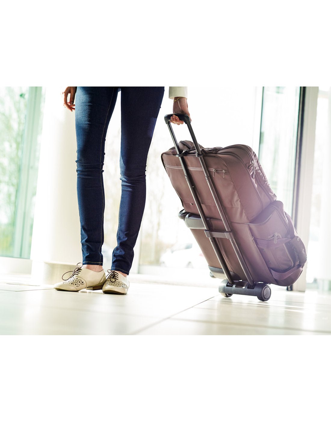 Lifestyle image of hand holding Go Travel Trolley at an angle, with handle extended and luggage placed on it. 