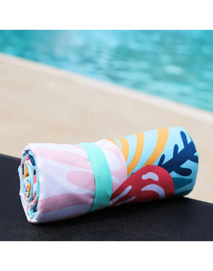 Lifestyle image of rolled up K5 Microfibre Beach Towel, positioned on a chair with pool visible in the background.