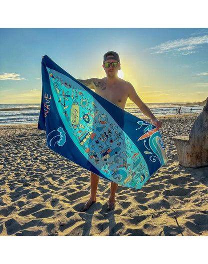 Lifestyle image of man holding surf K5 Microfibre Beach Towel diagonally, with beach visible in the background.