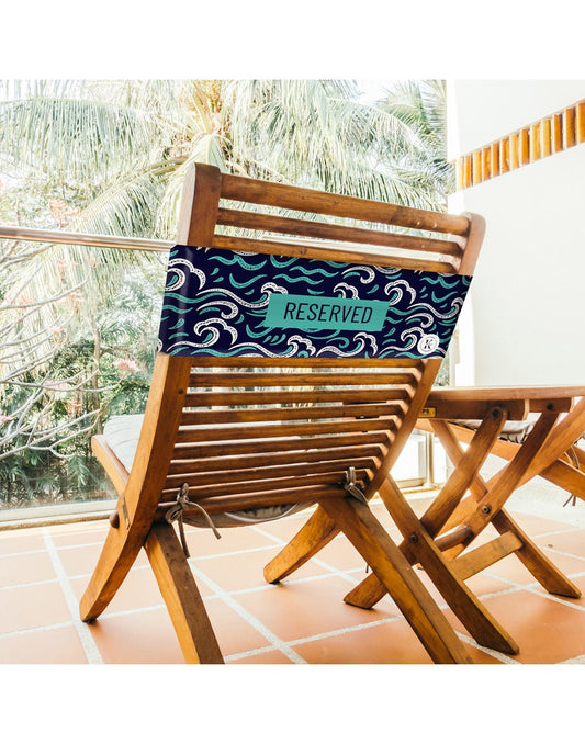 Product Image – Lifestyle image of ocean K5 Reserved Chair Sleeve, placed on a outdoor wooden chair with trees visible in the background.