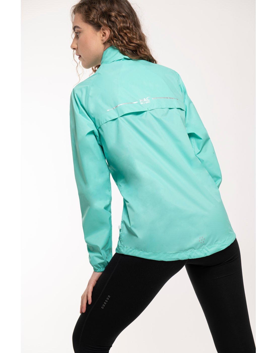 Back view of woman wearing Mac in a Sac Origin II Packable Waterproof Jacket in tiffany, with legs bent and hand resting on thigh.