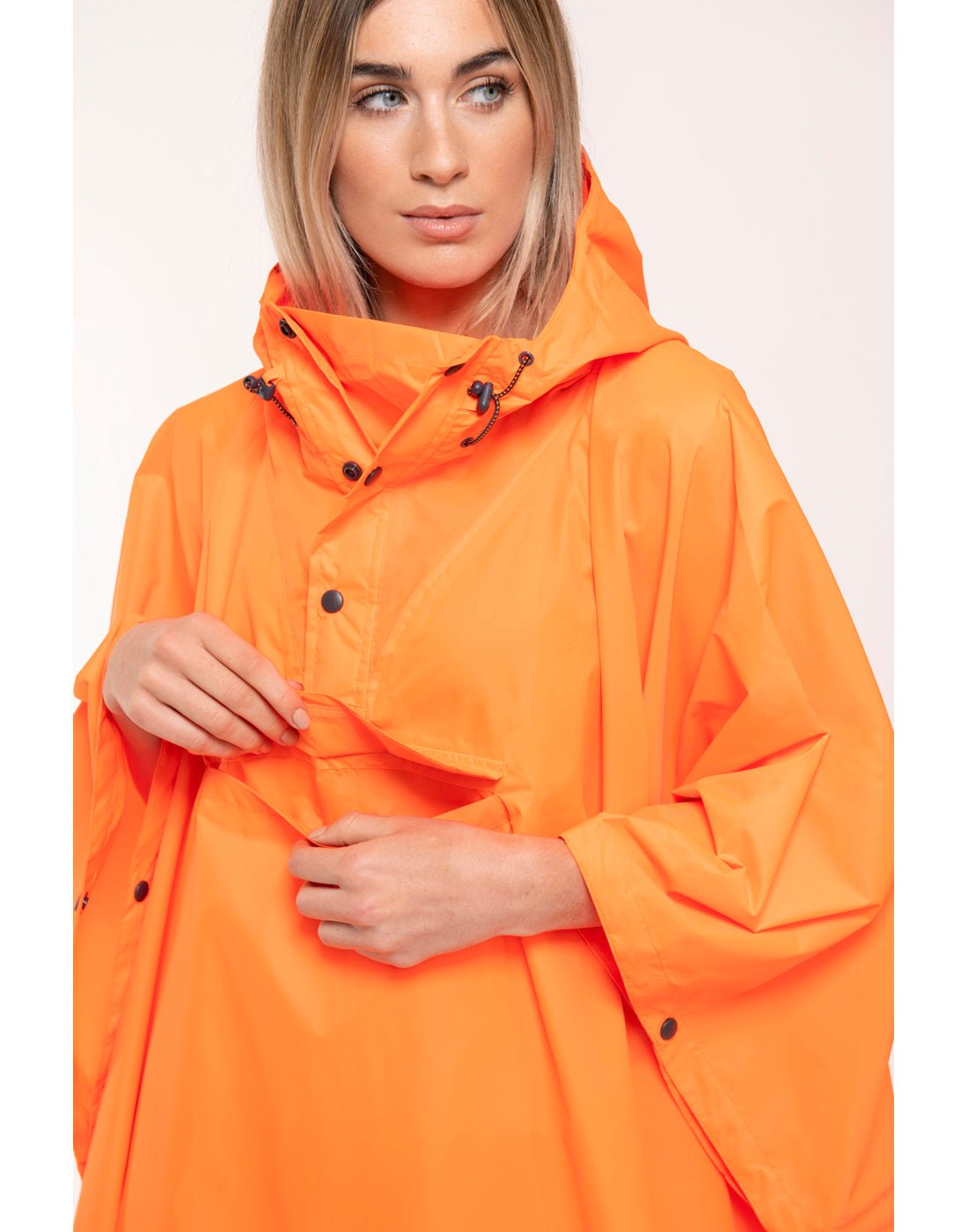 Front view of woman wearing Mac in a Sac Packable Waterproof Poncho in neon orange, opened pocket showing interior storage space.