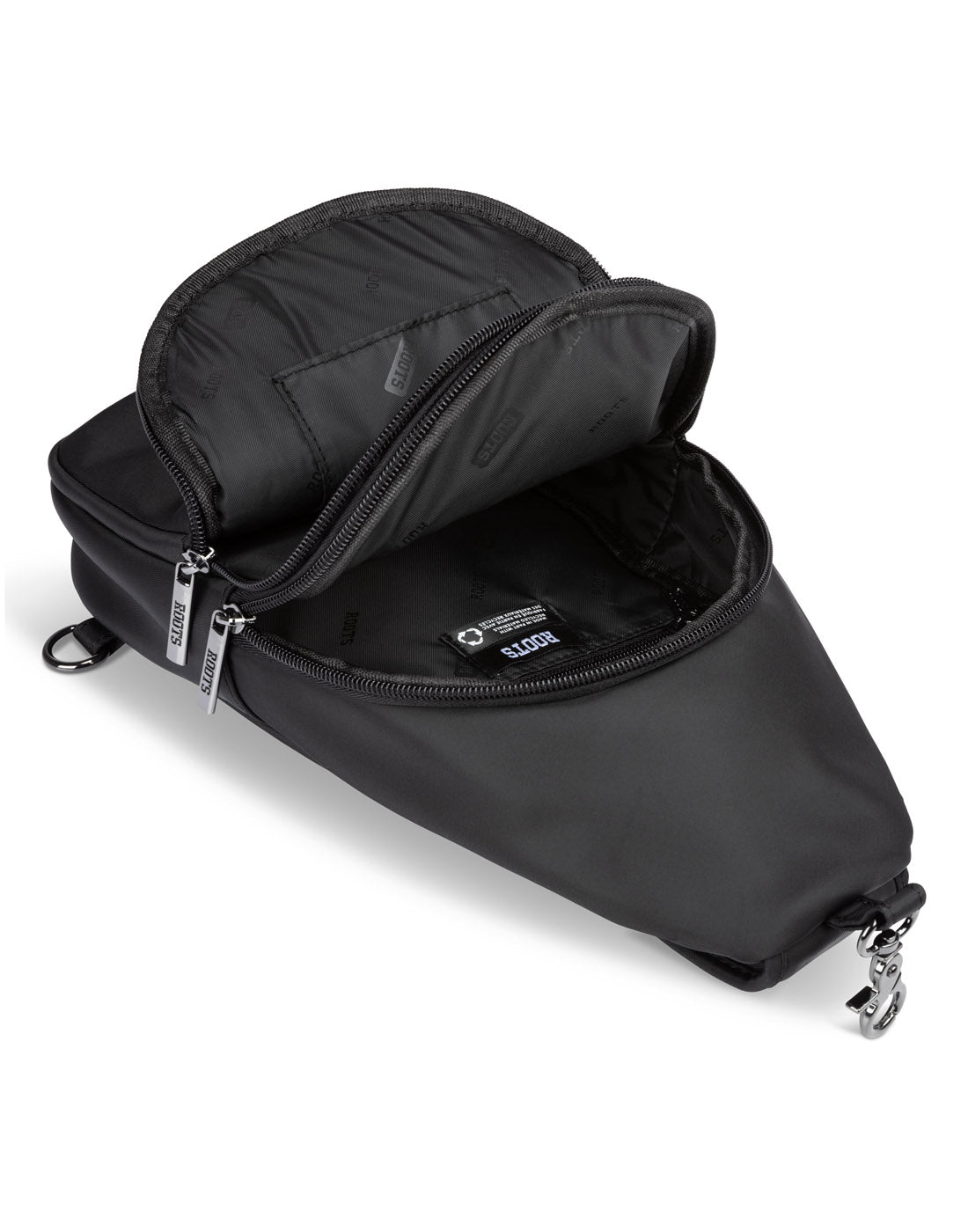 Angled view of unzipped Roots Travel Sling Bag in black, laying flat to show interior storage compartments.