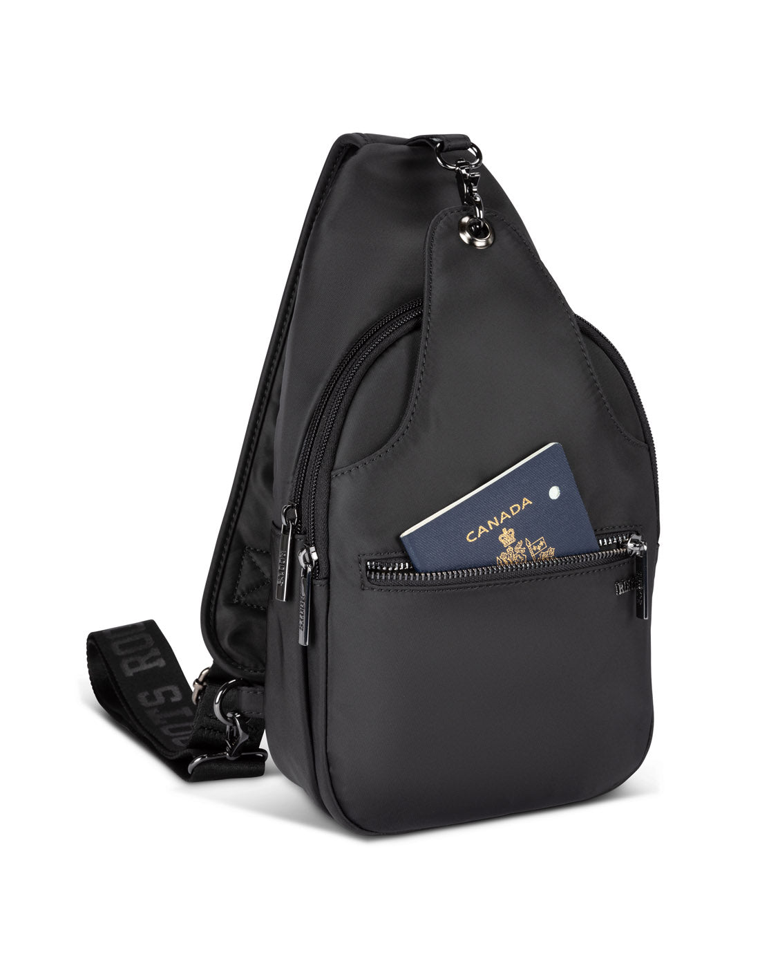 Front angle view of Roots Travel Sling Bag in black, with front pocket unzipped and a passport placed inside.