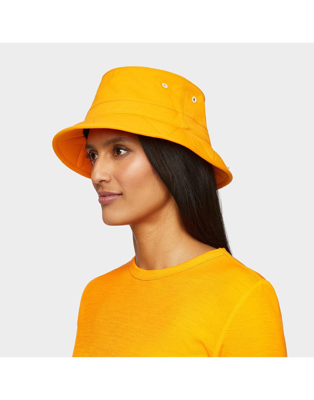 Portrait image of woman wearing Tilley Tofino Bucket Hat in bright orange with matching shirt, side angled view