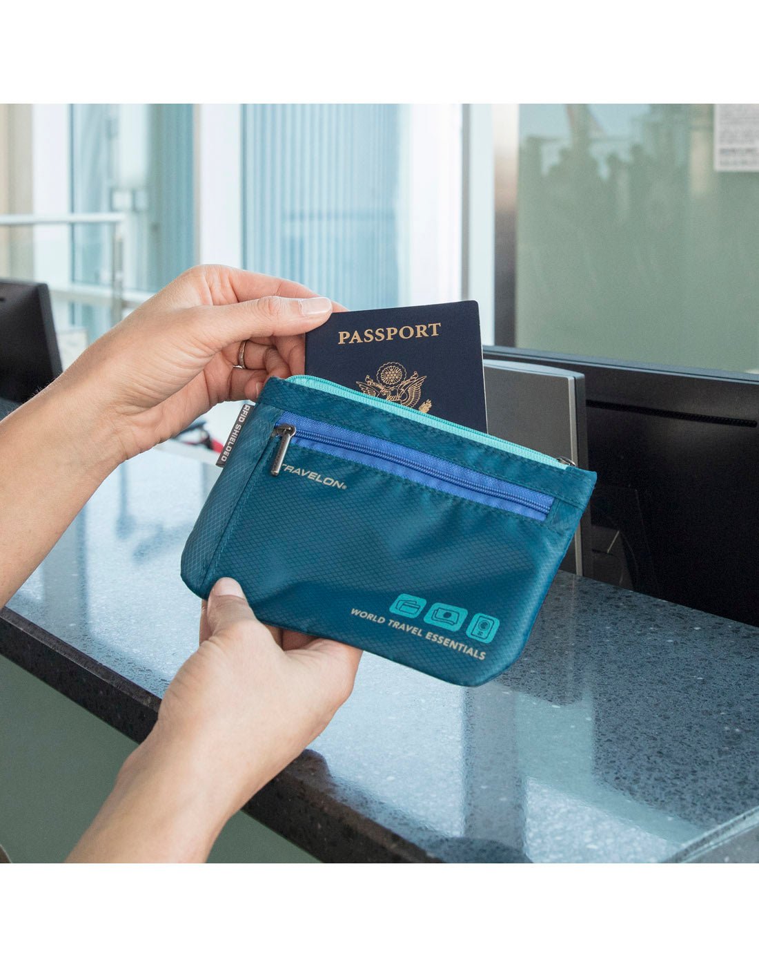 Lifestyle image of hands holding Travelon World Travel Essentials Set of 2 Currency & Passport Organizers in peacock teal, with one hand taking out passport in front of airport check-in desk. 