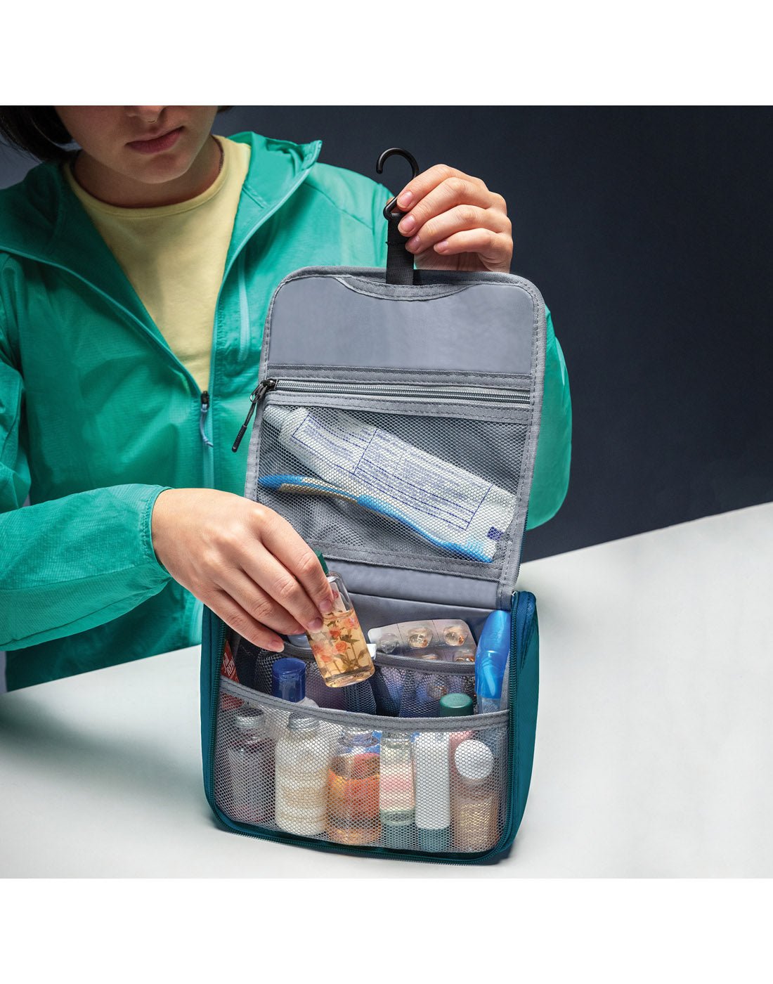 Lifestyle image of women storing items in unzipped Travelon World Travel Essentials Toiletry Bag in peacock teal.