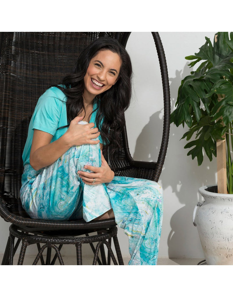Woman sitting on a wicker chair wearing Howard's Essential V-Neck T-Shirt in surf green and the Howard's Essential Lounge Pant in Light Blue Marble