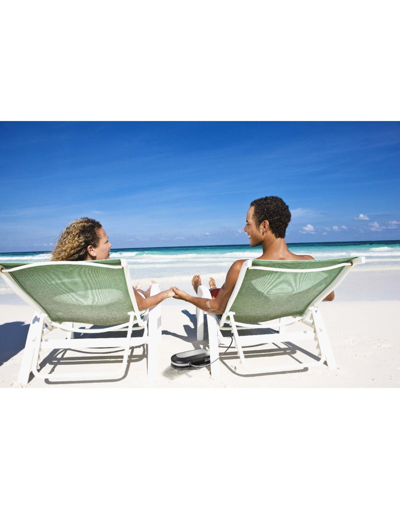 Woman and man sitting on lounge chairs at the beach with the Master Lock® Set-Your-Own-Combination Portable Safe tethered to one of the chairs