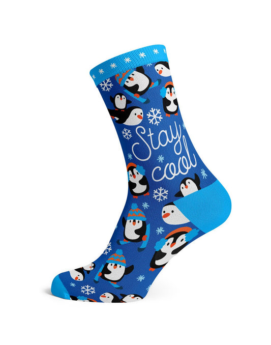 Product Image – One royal blue sock with light blue toe, heel and cuff with white snowflakes and many penguins some wearing blue and orange toques or earmuffs or skiis with words Stay Cool in white script font