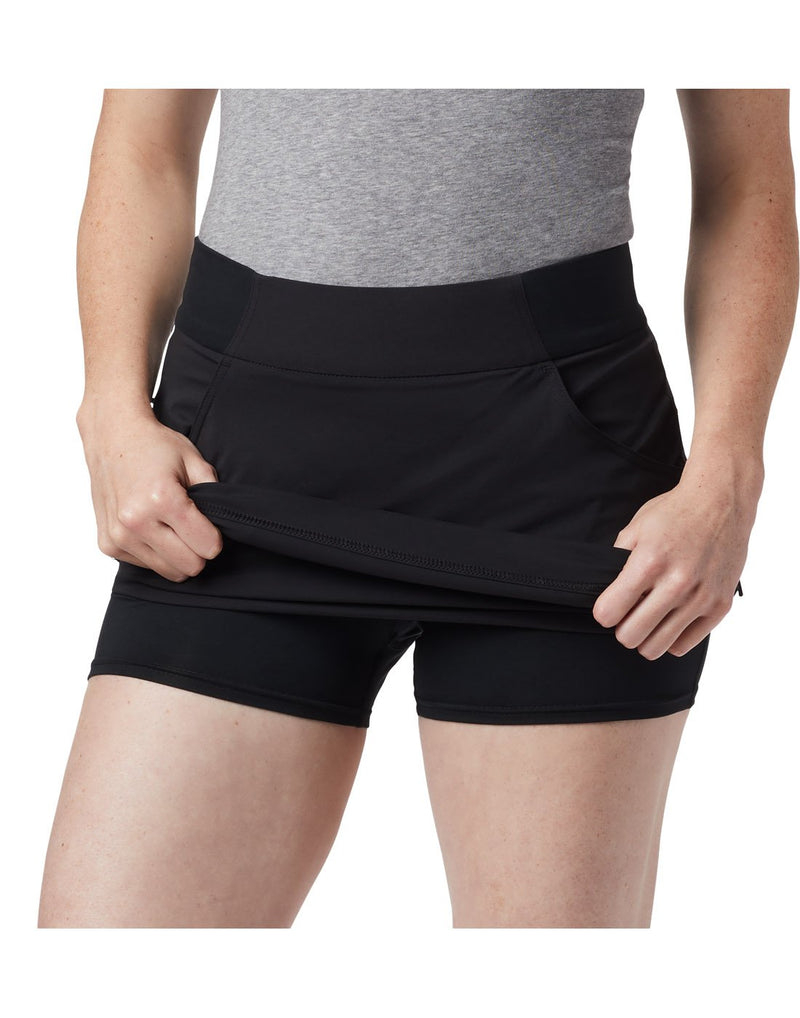 Woman wearing Columbia Women's Anytime Casual™ Skort - black, front view holding skirt part up to show shorts underneath
