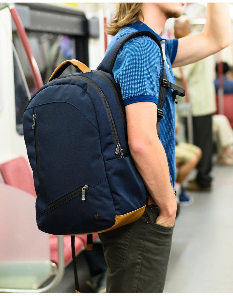 Man wearing navy PKG Durham II Backpack slung on one shoulder, riding subway