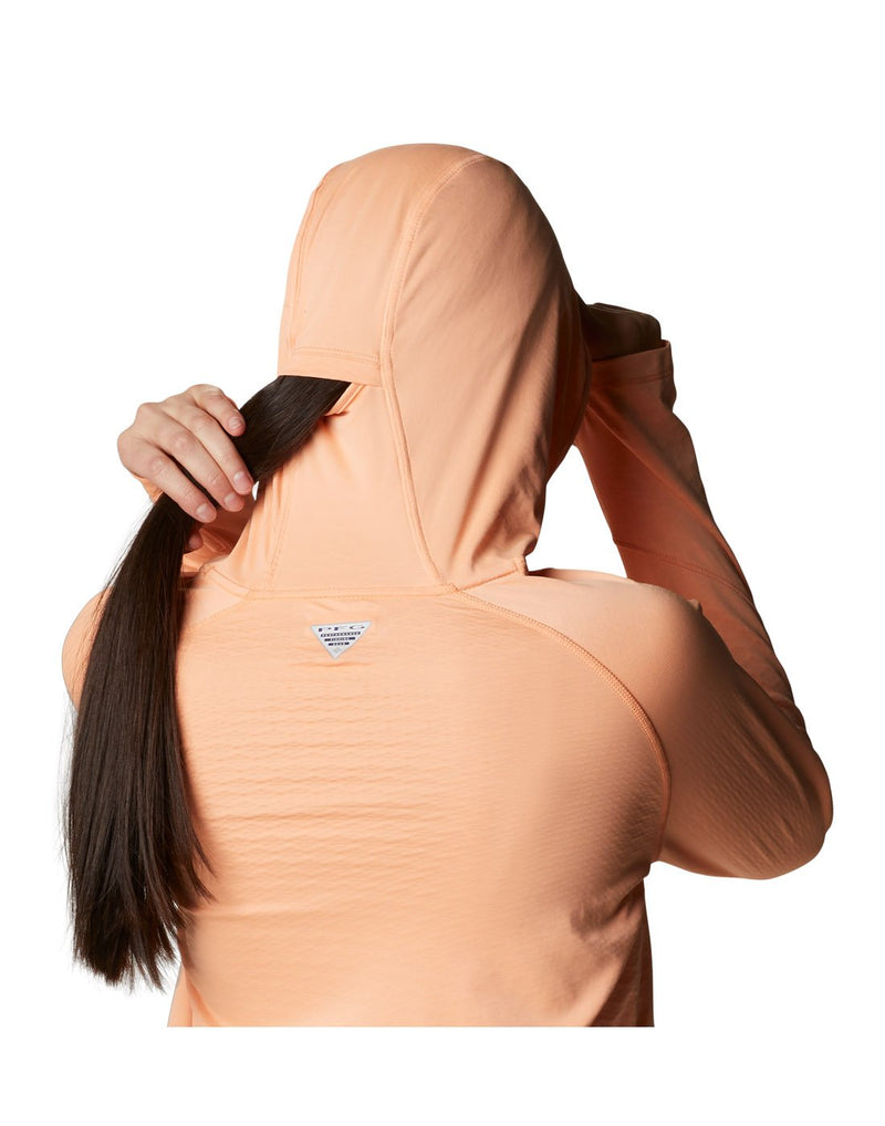 Close up of woman wearing Columbia Women's PFG ZERO Rules™ Ice Hoodie - bright nectar colour, showing back of head, pulling a ponytail through the hood slit
