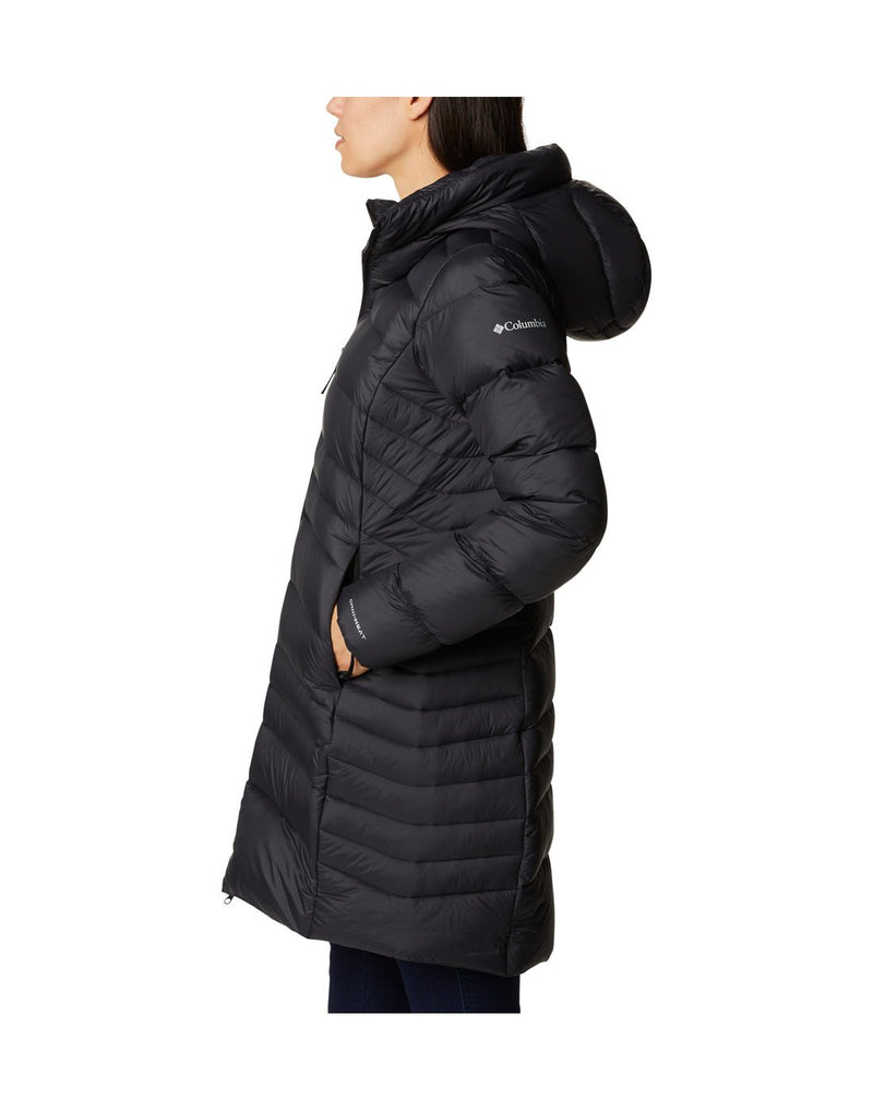 Woman wearing Columbia Women's Autumn Park™ Down Hooded Mid Jacket in black, with hands in pockets, side view with Columbia logo on left shoulder