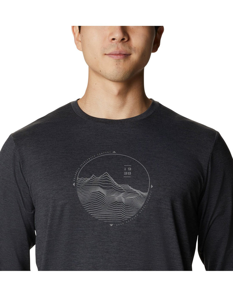 Close up of man wearing black heather Columbia Men's Tech Trail™ Long Sleeve Graphic T-Shirt with circular graphic of mountains