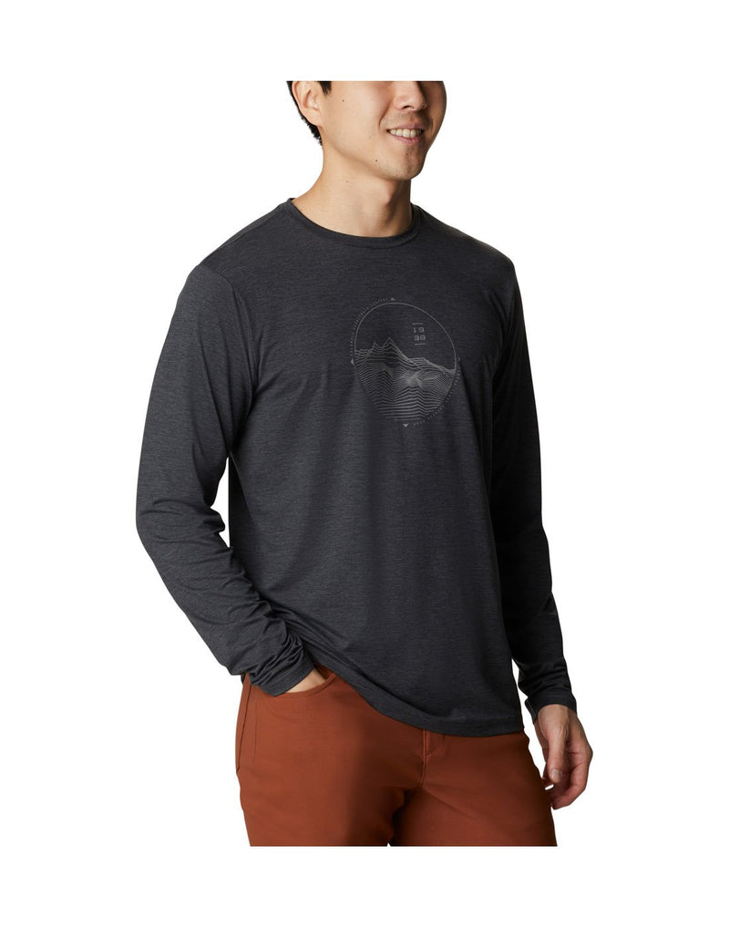 Man wearing Columbia Men's Tech Trail™ Long Sleeve Graphic T-Shirt in black heather, angled front view with right hand in his pocket