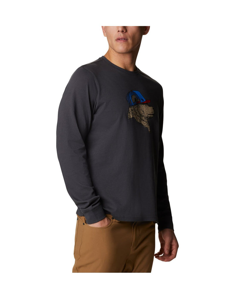 Man wearing Columbia Men's Apres Lifestyle™ Long Sleeve Graphic T-Shirt in shark colour with graphic of dog wearing a ball cap, angled front view with right hand in pocket