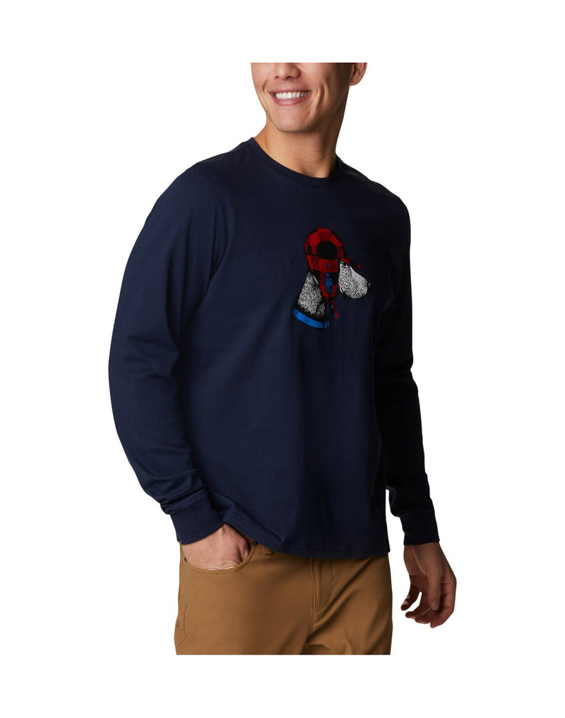 Man wearing Columbia Men's Apres Lifestyle™ Long Sleeve Graphic T-Shirt in collegiate navy colour with graphic of dog wearing a winter hat, angled front view with right hand in pocket