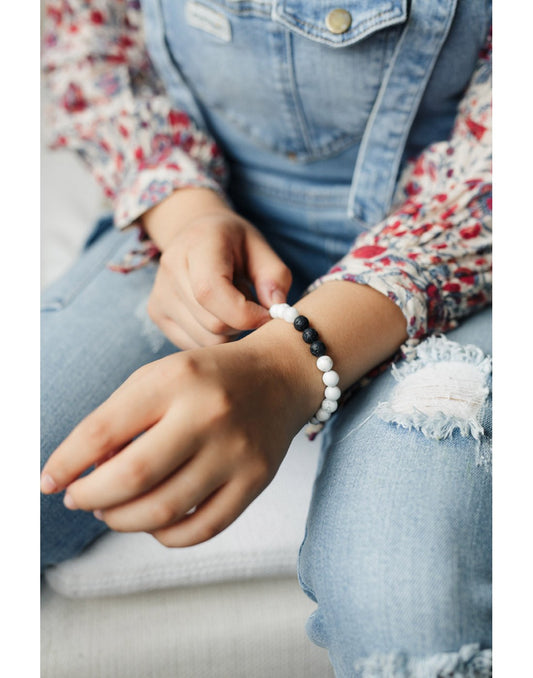 Product Image – Woman wearing floral shirt and denim overalls wearing the Fern & Petal White-Howlite Bracelet