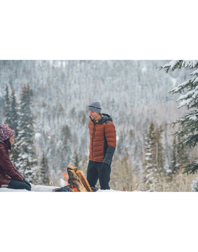 Man standing infront of a campfire wearing orange winter jacket and city grey heather Columbia Stuart Island™ Omni-Heat™ Infinity Watch Cap outside in winter with snow covered pine trees around