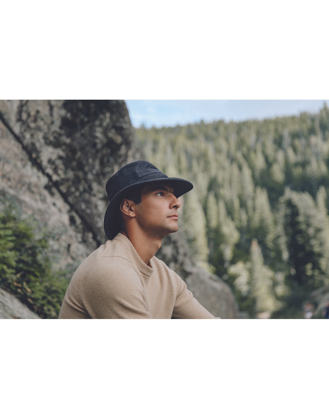 Man wearing a beige sweater and the Tilley TTW2 Tec Wool Hat in black, side view on an outdoor vantage point looking out to trees and mountain side