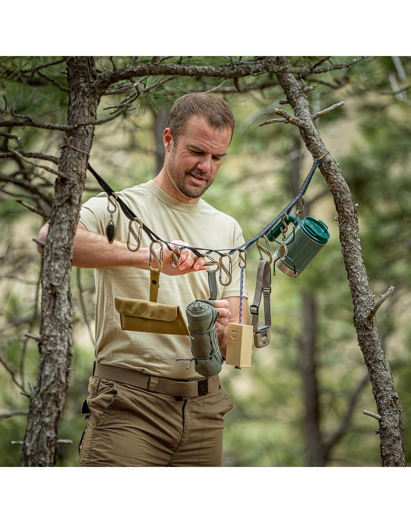 Man in wilderness with Nite Ize Gearline® Organization System attached between two trees with various outdoor gear clipped