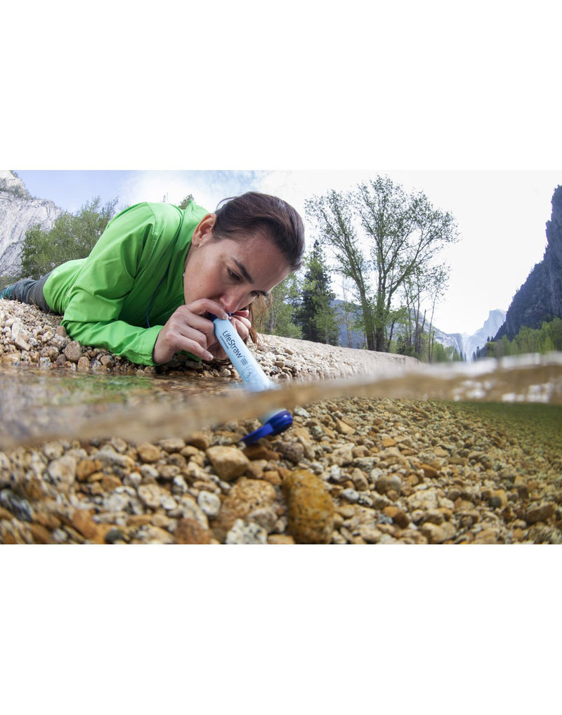 Woman laying down near water drinking with the LifeStraw Personal Water Filter directly from water source