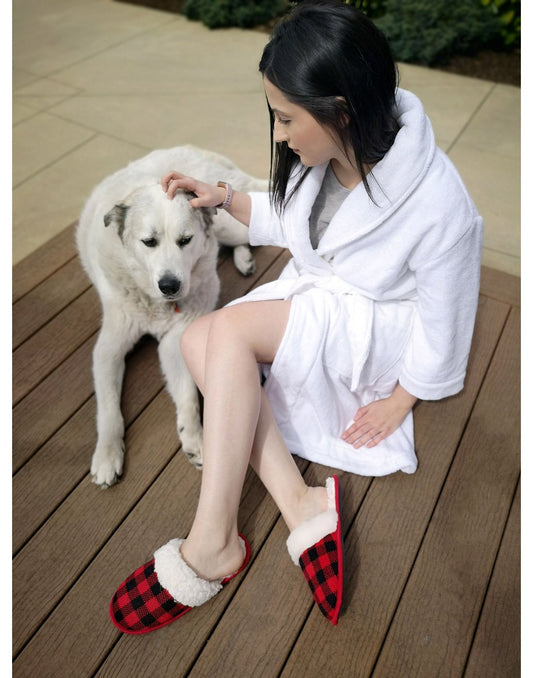 Product Image – Woman wearing white robe and Pudus Creekside Slide Slippers in Lumberjack Red, sitting on a deck petting a white dog