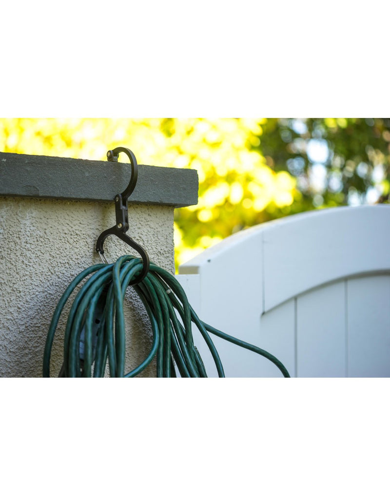 Garden hose attached to the medium Heroclip and hooked on the side of a small cement wall, next to a gate