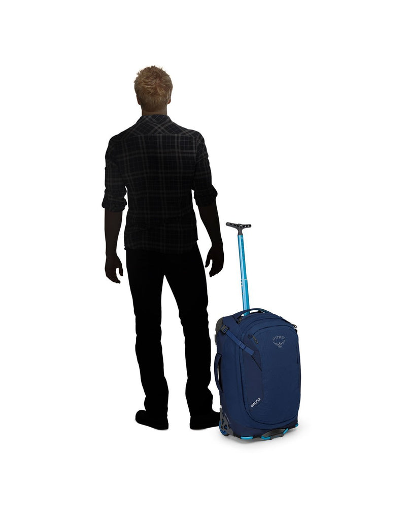 Man standing beside osprey ozone 42L/21.5" buoyant blue colour luggage bag front view