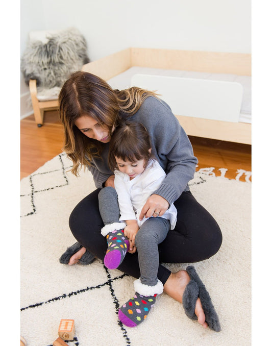 Product Image – Mother sitting cross-legged on a white carpet with daughter sitting on her lap wearing Pudus Kids Classic Slipper Socks in Polka Dot Multi 