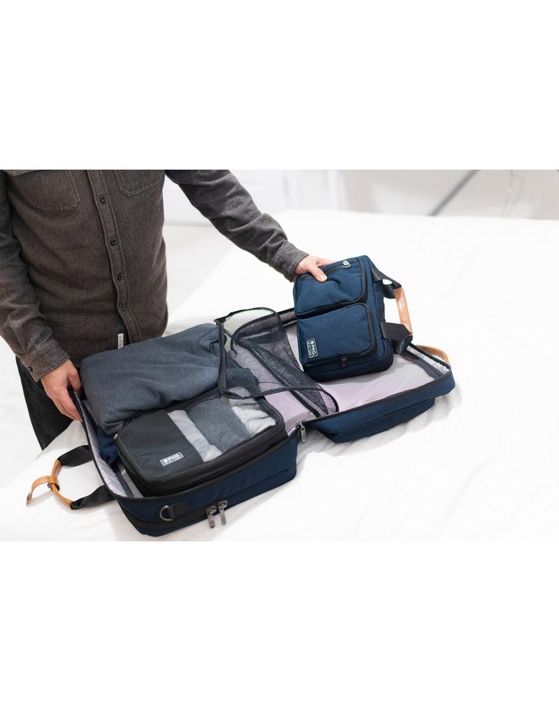 Person packing navy PKG Simcoe Hanging Dopp Kit into a suitcase on a bed