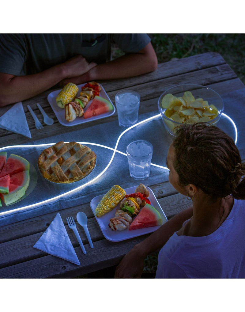 Nite Ize Radiant® Rechargeable Shineline™ laid out around some food on a picnic table with two people ready to eat