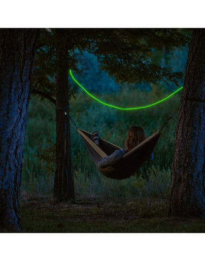 Person laying in a hammock between trees with a green Nite Ize Radiant® Rechargeable Shineline™ stretched across the trees