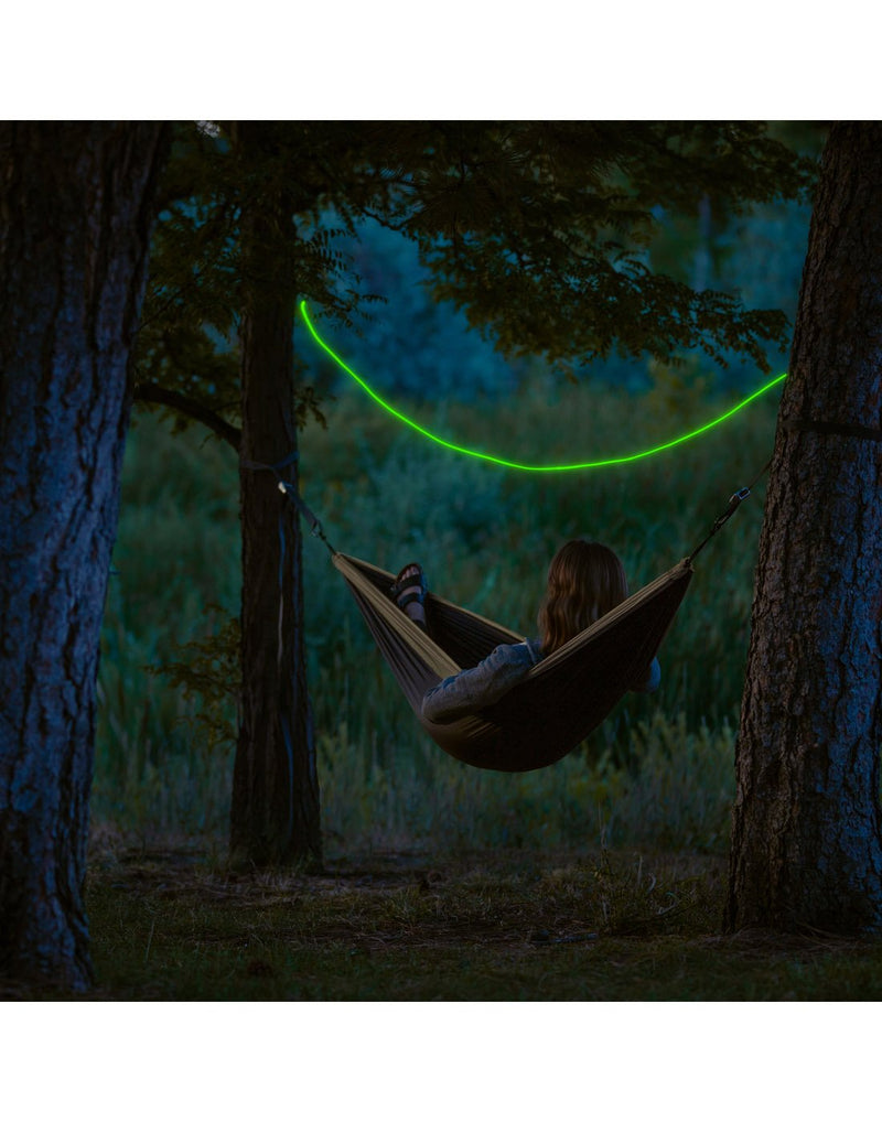 Person laying in a hammock between trees with a green Nite Ize Radiant® Rechargeable Shineline™ stretched across the trees