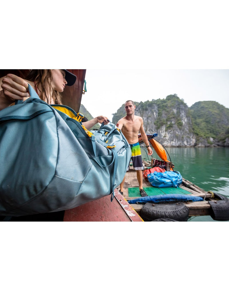 Women carrying osprey transporter 65 expedition keystone grey colour duffle bag corner view