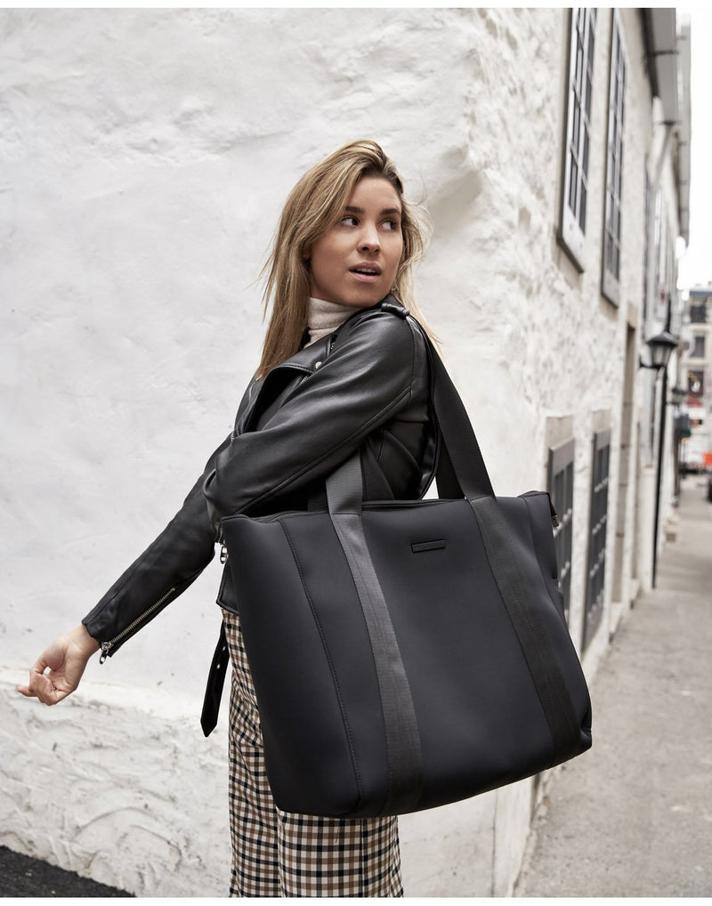Woman standing on a street wearing a leather jacket with the MyTagAlongs Weekender tote slung on her left shoulder